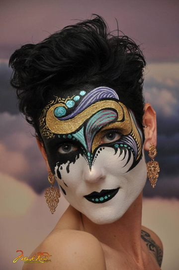 Body and face painter Monique Lily in an intricate face paint that features green and purple swirls and a white lower face